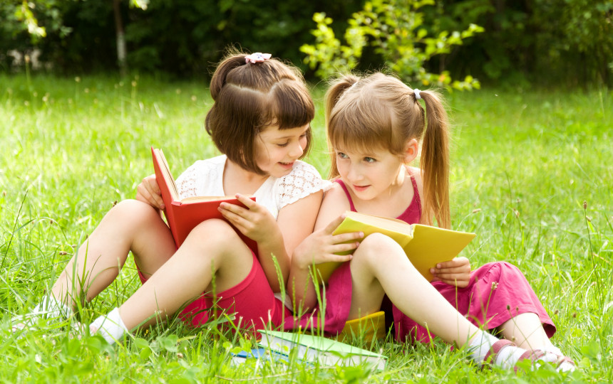 Little girl sisters. Reading girls Pink. Little in skirt on grass. Two girls Lie on the grass and talk. Two girls sitting on the Lawn.